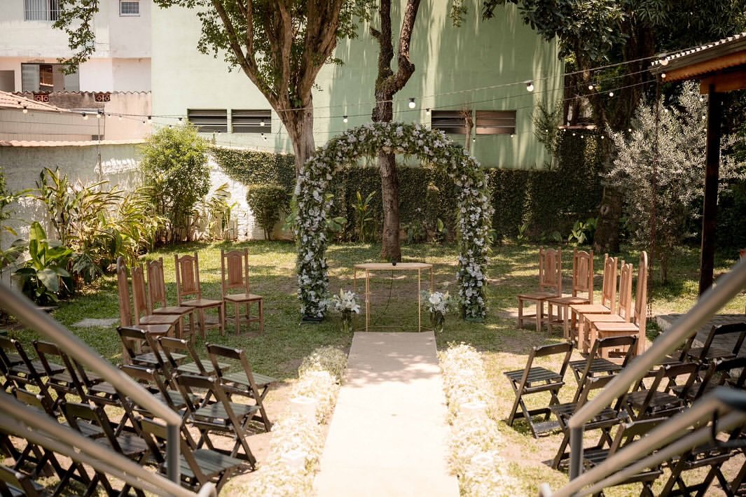 Cerimônia ao ar livre com arco de flores brancas e cadeiras dispostas no jardim