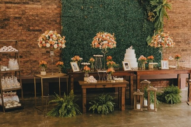 Mesa de bolo rústica com muro verde e arranjos florais em tons pêssego